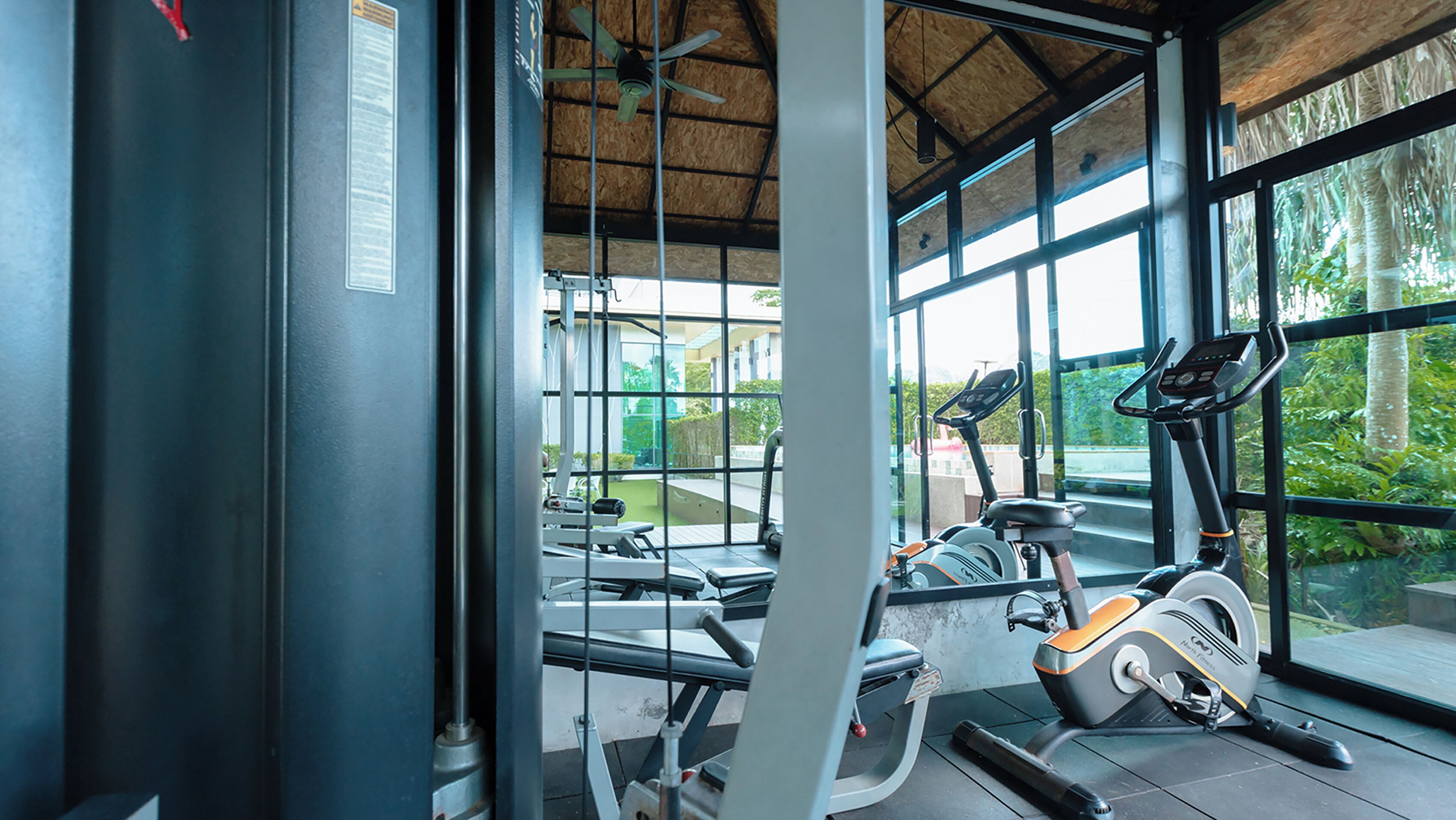 A gym with exercise equipment, large windows, and a view of greenery outside.
