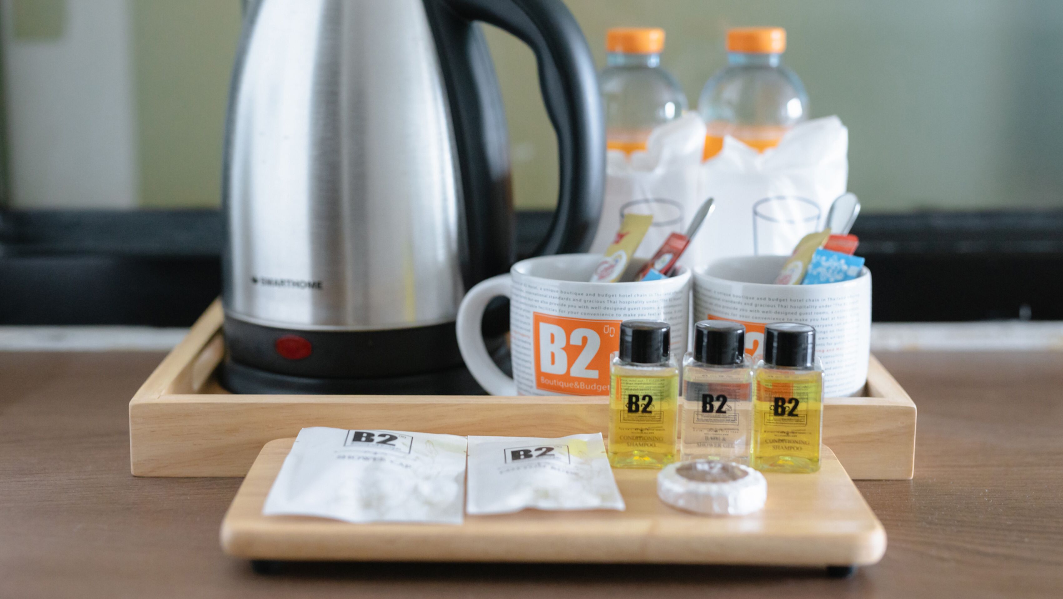 A tray with toiletries including B2 branded shampoo, conditioner, and a toothbrush, a kettle, and a mug with B2 branding.