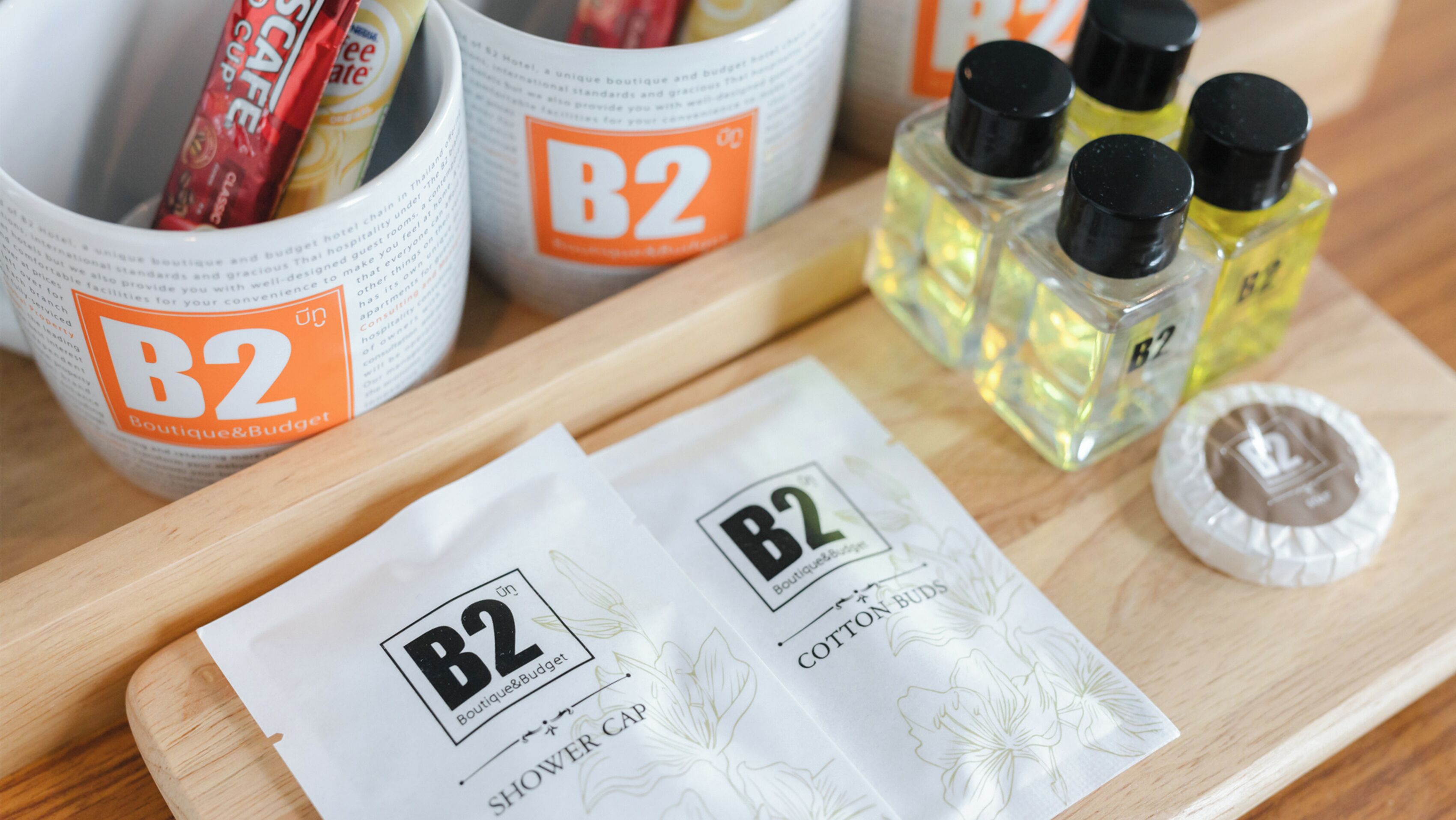 En træbakke med produkter fra B2 Boutique & Budget, herunder en badehætte og vatpinde.