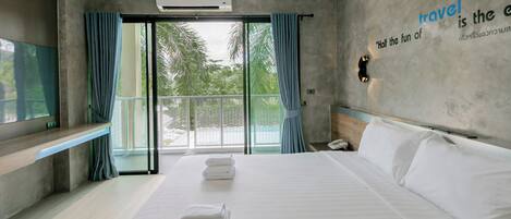 A modern hotel room with a bed, a TV, a balcony with curtains, and a wall with a travel quote.