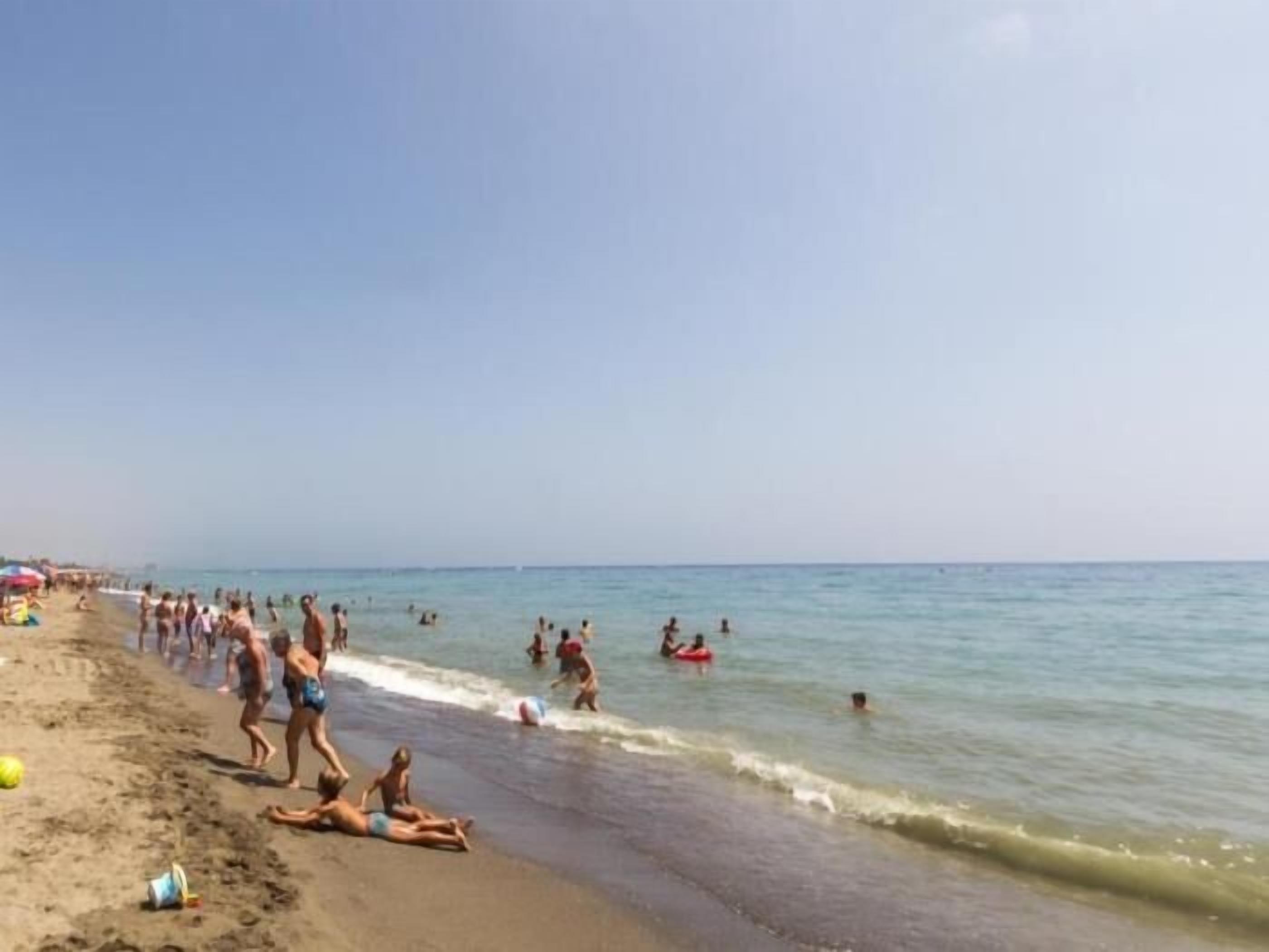 A crowded beach with people swimming and playing in the water.
