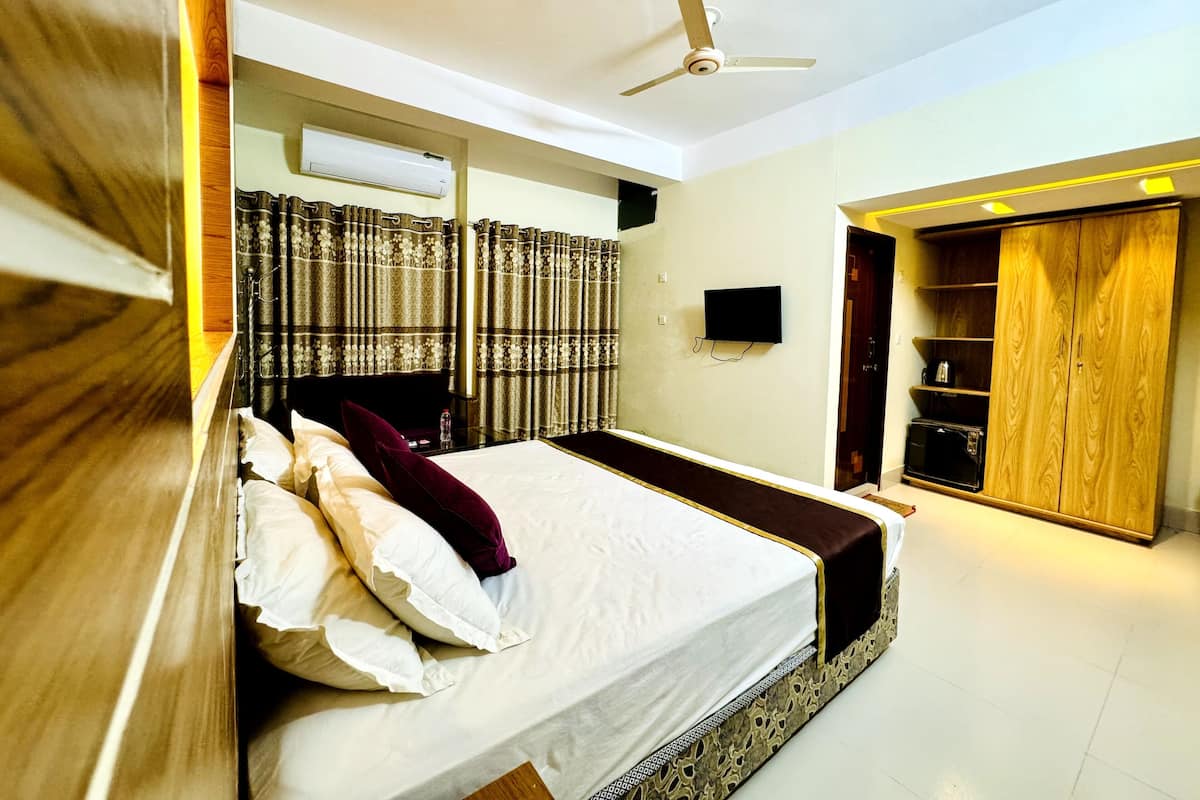 A bedroom with a bed, curtains, a ceiling fan, a TV, and a wardrobe.