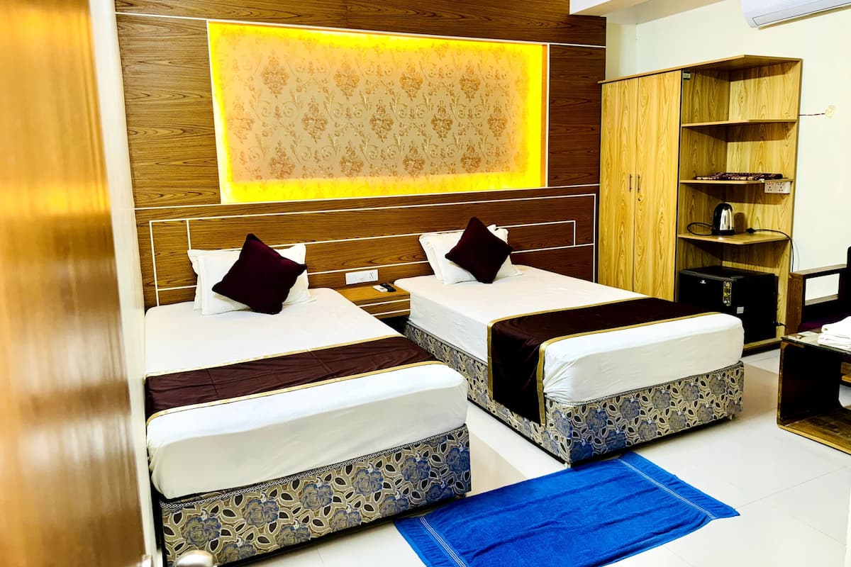 A hotel room with two beds, a large mirror, a wardrobe, and a desk with a kettle.