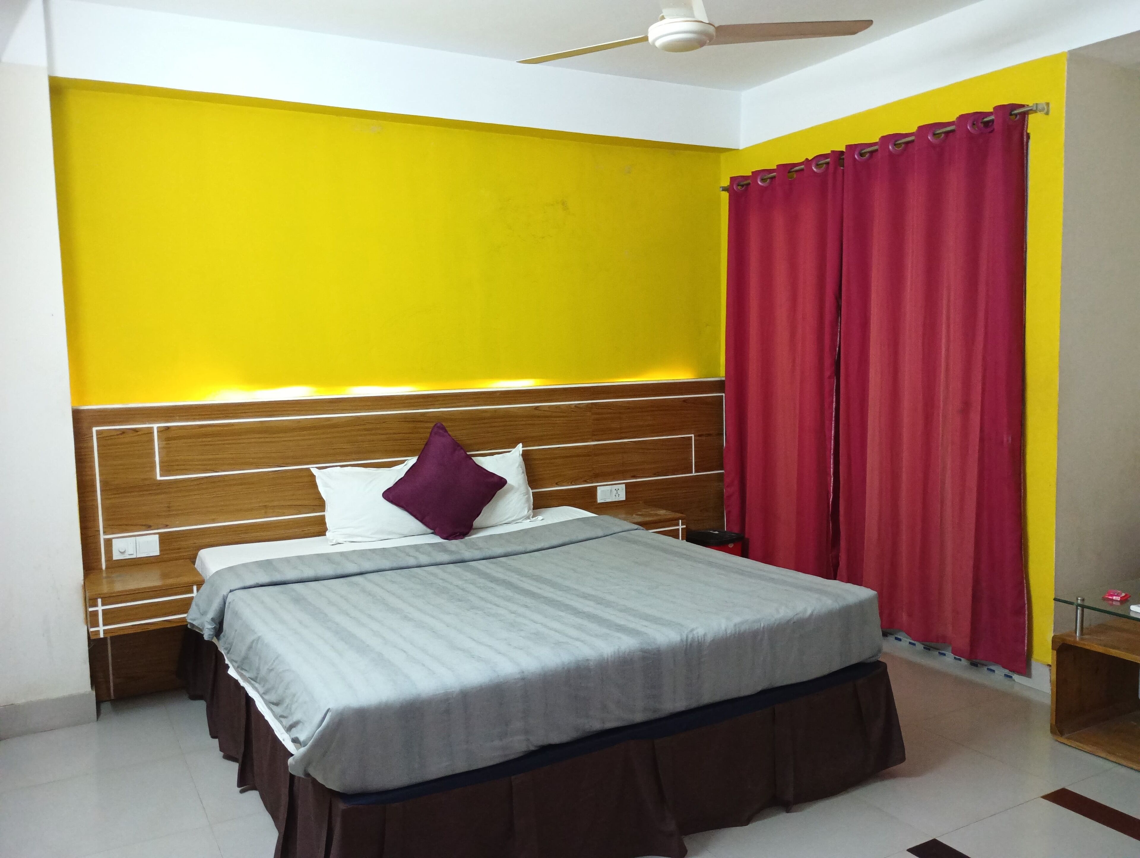 Una habitación de hotel con una cama, cabecero de madera y cortina roja.