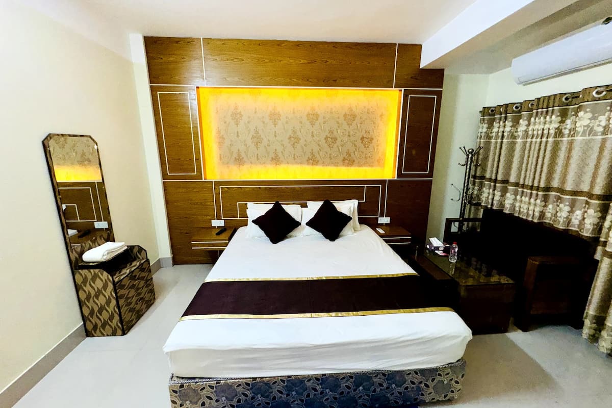A hotel room with a large bed, a bedside table, a mirror, and a desk with a chair.