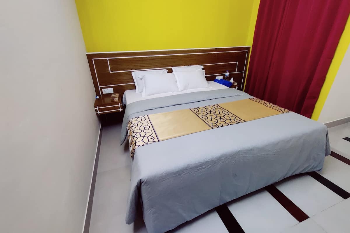 A hotel room with a bed, a nightstand, and a red curtain.