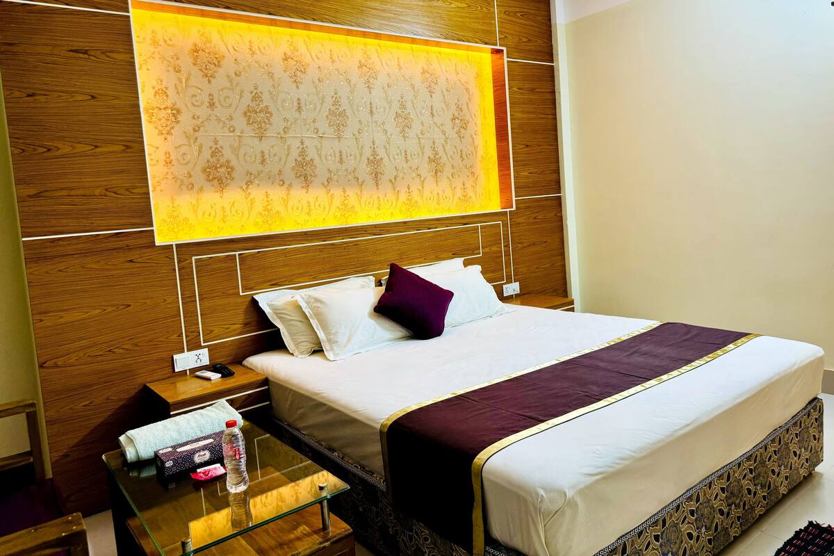 A hotel room with a large bed, a nightstand with a lamp, and a glass table with a bottle of water.