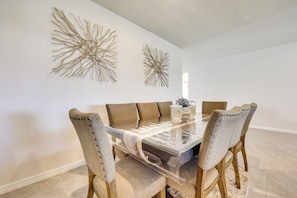 Un comedor con una mesa de vidrio, sillas tapizadas en tono beige y dos elementos decorativos colgados en la pared.