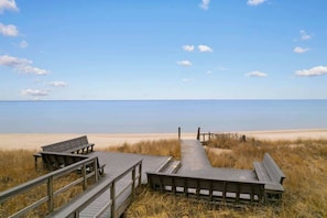 Una passerella in legno che conduce a una spiaggia sabbiosa, con panchine.