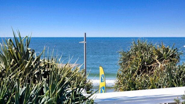 A beach view with a surfboard and a lifeguard stand. - Ocean View Haven at Paradiso (Kingscliff)