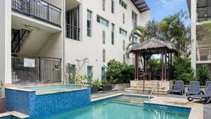 A pool area with a blue-tiled edge, a thatched-roof gazebo, and lounge chairs. - Ocean View Haven at Paradiso (Kingscliff)