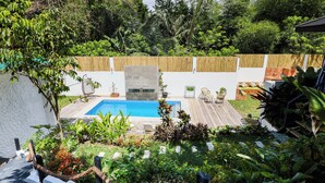 Un patio trasero con piscina, terraza de madera y diversas plantas.