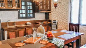 Un comedor con una mesa de madera, individuales y un cuenco de fruta. Hay armarios de madera y una ventana sobre la mesa.