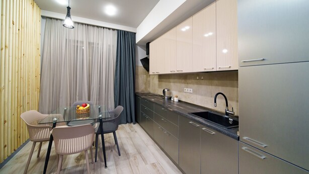 A modern kitchen with a dining area, featuring a glass table, two chairs, a fruit basket, and a sink. - Rooftop Cityview Apartment by Sweet Home (Yerevan)