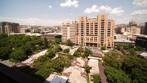 A high-rise building with multiple balconies, surrounded by trees and other buildings.