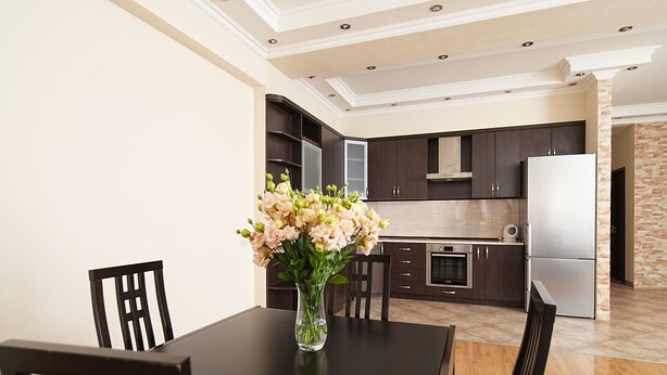 A modern kitchen with dark cabinets, a stainless steel refrigerator, and a vase of flowers on the dining table.