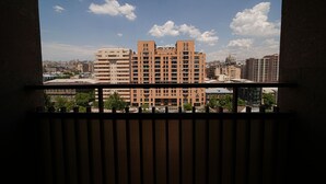 A view from a balcony with a metal railing, overlooking a cityscape with multiple high-rise buildings and a clear sky.