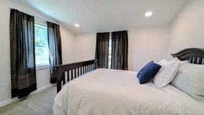 Un dormitorio con una cama grande, cortinas oscuras, cabecero de madera y vistas a la vegetación exterior.