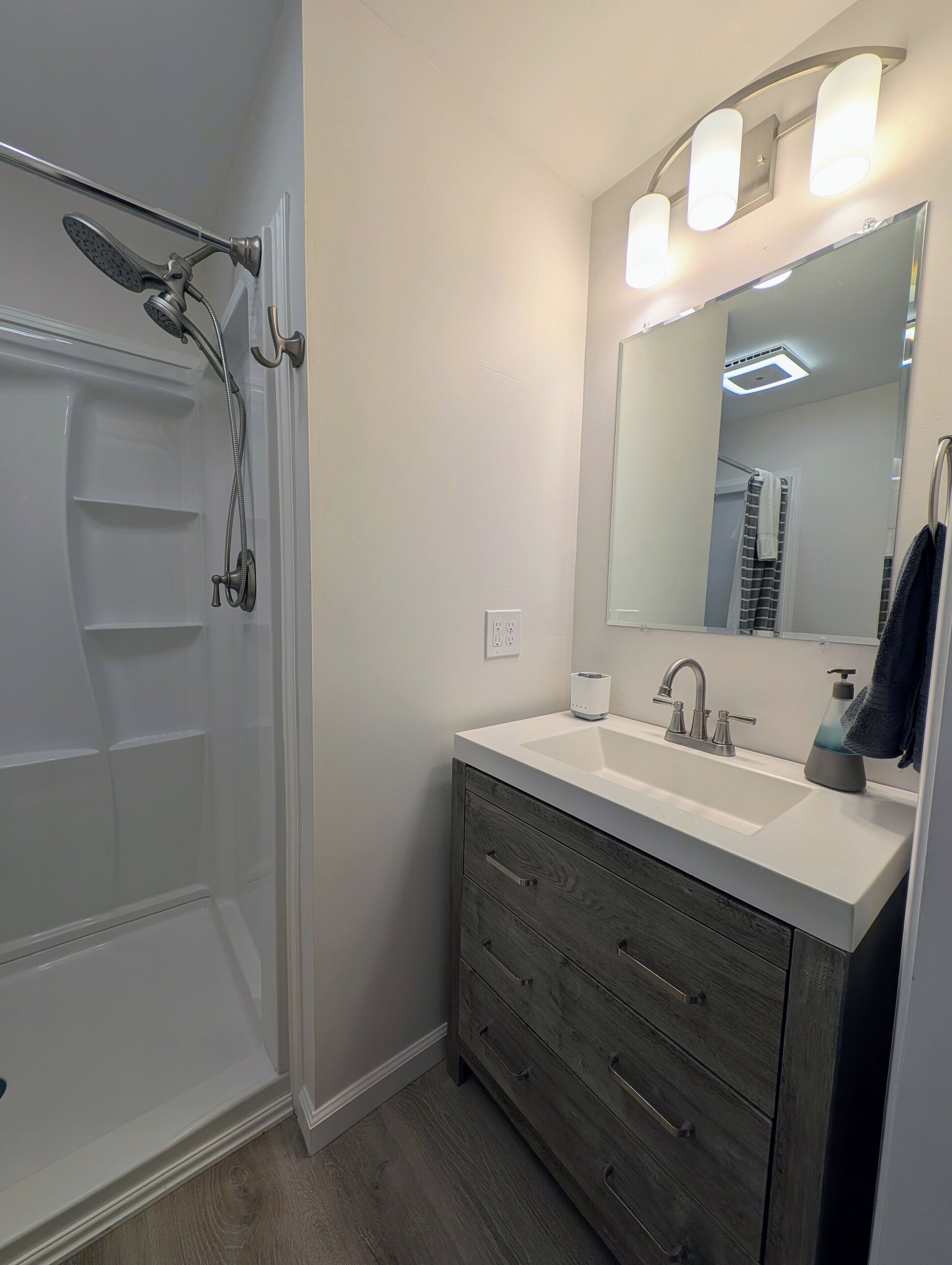 A bathroom with a shower, a sink, a mirror, and a vanity with drawers.