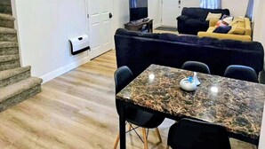 Una sala de estar moderna con comedor, que incluye una mesa de mármol, sillas negras, un sofá y un televisor.
