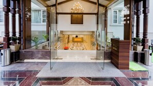 Um saguão de hotel com entrada de vidro, um candelabro e um balcão de recepção.