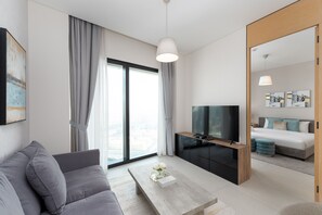 Un salon moderne avec un canapé, une table basse, un téléviseur et une grande fenêtre avec des rideaux.