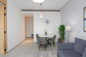 Un salon moderne avec un canapé gris, une table de salle à manger ronde entourée de quatre chaises, une plante en pot et un luminaire suspendu.