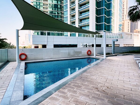 A swimming pool with a tiled deck, surrounded by high-rise buildings.