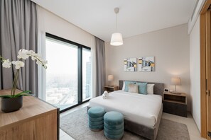 A modern hotel room with a large bed, two bedside tables, a view of the city, and a potted orchid.