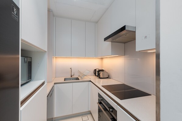 Una cocina compacta con armarios blancos, horno integrado, microondas y tostadora.