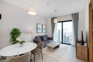 A modern living room with a dining area, a grey sofa, a coffee table, and a large window with a city view.