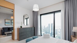 Una habitación de hotel moderna con una cama grande, vistas a la ciudad, un sofá gris y una pequeña mesa con una planta en maceta.