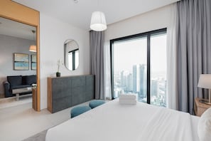 Une chambre d’hôtel moderne avec un grand lit, une vue sur la ville, un canapé gris et une petite table sur laquelle est posée une plante en pot.