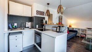Una cocina moderna con armarios blancos, horno integrado y lavamanos. Hay una zona de comedor con un sofá y una mesa de centro de vidrio.