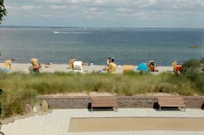 Una playa con gente relajándose, un banco y vista al mar.