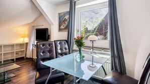Una habitación moderna con una mesa de vidrio, sillones de cuero, un televisor y una ventana con cortinas.