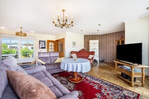 A living room with a sectional sofa, a round table, a TV stand, and a brick wall.