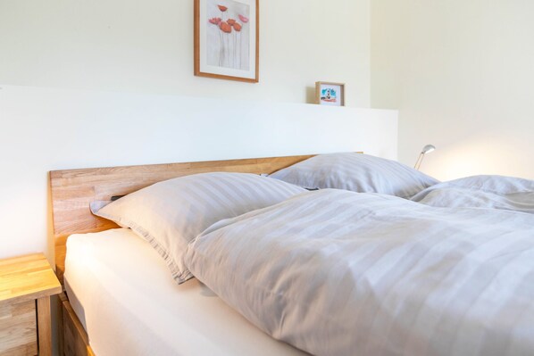 Una cama bien hecha con cabecera de madera, una mesita de noche y un cuadro colgado en la pared.