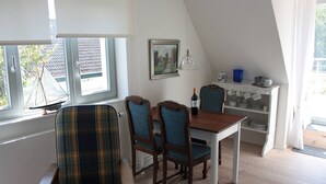 A dining area with a table and chairs, a window with a view, a shelf with dishes, and a hanging lamp.