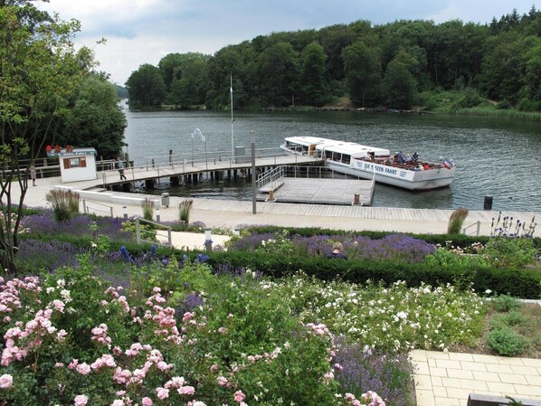 Un quai au bord de la rivière, avec un bateau amarré, entouré d’une végétation luxuriante et de plantes en fleurs.