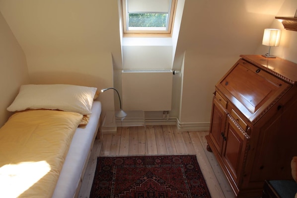 Een slaapkamer met een bed, een radiator, een raam, een lamp, een kast en een vloerkleed.