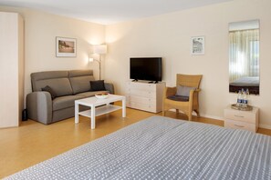 Moderni hotellihuone, jossa on sohva, televisio, rottinkituoli ja sänky.