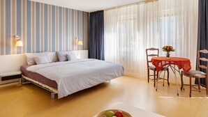 Ett hotellrum med en säng, ett sängbord, ett matbord med stolar och en skål med frukt på bordet.