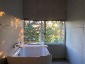Ein modernes Badezimmer mit einer Badewanne, einem Fenster und Blick auf Bäume.