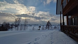 A snow-covered landscape with a wooden building featuring large windows and a balcony. - Biei san-ai-no-oka Villa Shion (Biei)