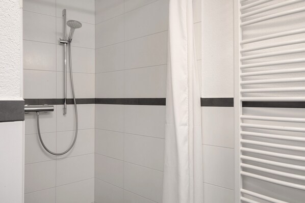 Una ducha con cabezal de ducha manual y grifo empotrado en la pared, un perchero y pared con azulejos blanco y negro.