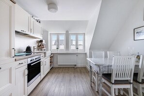A kitchen with white cabinets, a stove, and a dining table with chairs. - Apartment 'Fewo Samson' with Private Terrace, Shared Garden and Wi-Fi (Emmelsbüll-Horsbüll)