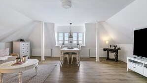 A spacious loft with a high ceiling, a dining table with chairs, a television, and a sewing machine. - Apartment 'Fewo Samson' with Private Terrace, Shared Garden and Wi-Fi (Emmelsbüll-Horsbüll)