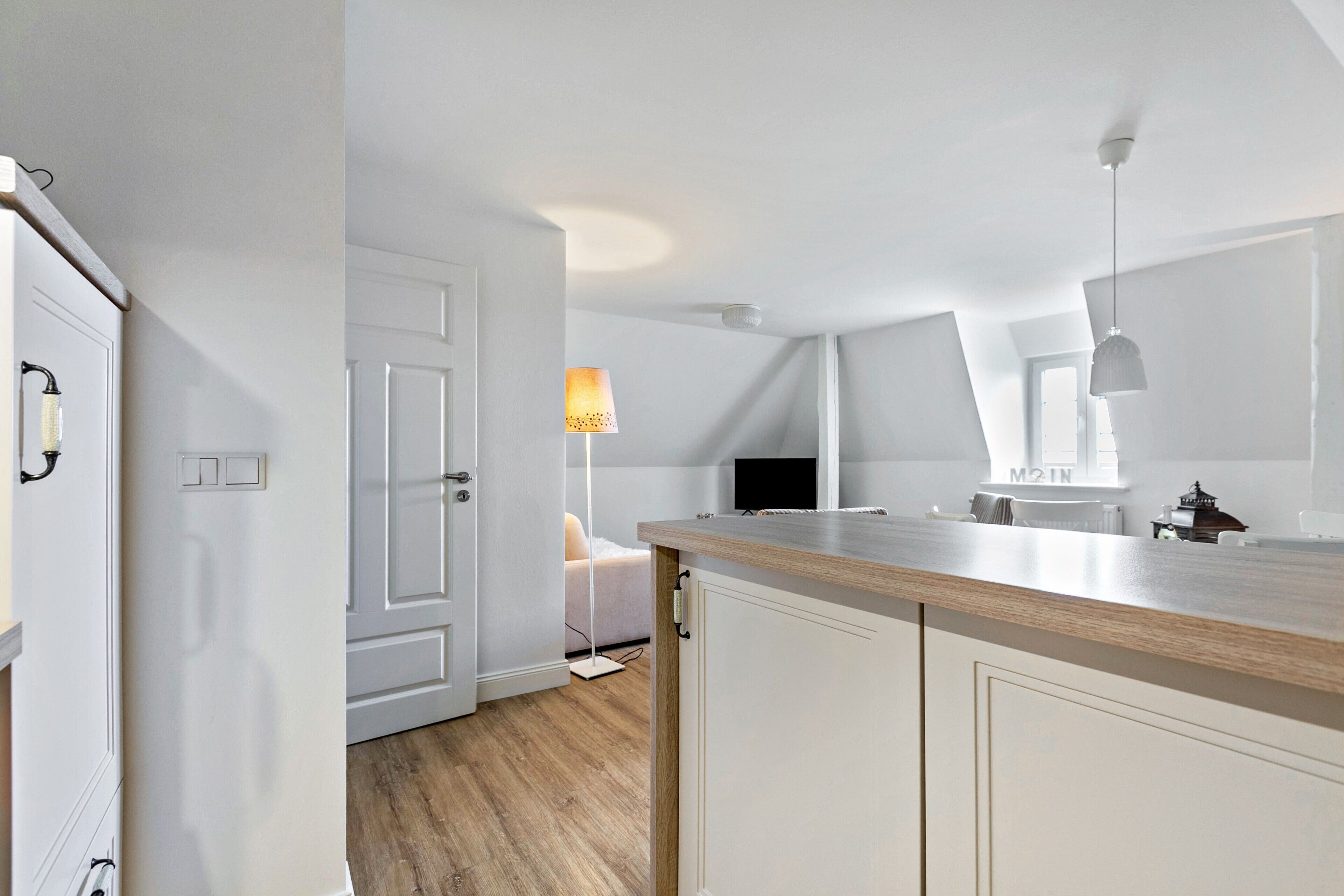 A modern kitchen with white cabinetry, a wooden countertop, and a pendant light.