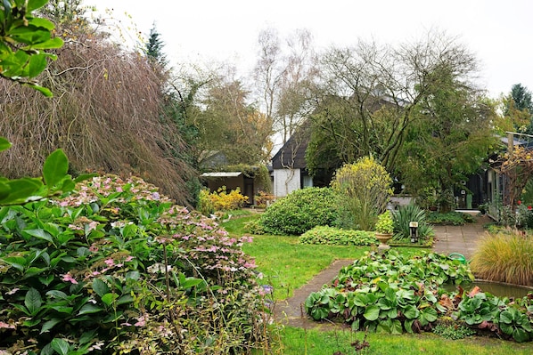 Un jardin avec un sentier menant à un bâtiment blanc, entouré de différentes plantes et de divers arbres.